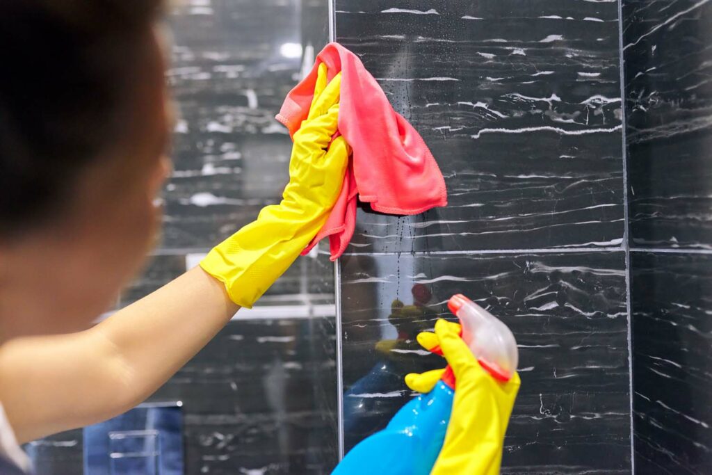 Bathroom cleaning, woman in gloves with rag polishing tiles