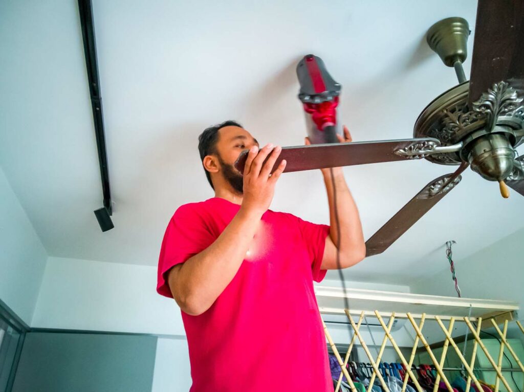 Cleaning the ceiling fan using vacuum cleaner.