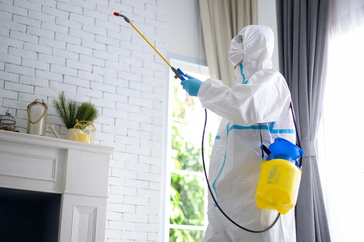 A medical staff in PPE suit is using disinfectant spray in living room, Covid-19 protection , disinfection concept